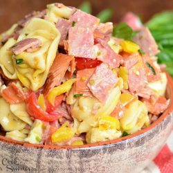 close up view of clay crock filled with italian tortellini salad on red and white cloths on a wooden table
