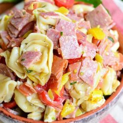 view from above of clay crock filled with italian tortellini salad on red and white cloths on a wooden table