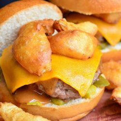 Onion ring bbq cheeseburger on a wooden table with hand battered and fried onion rings in foreground