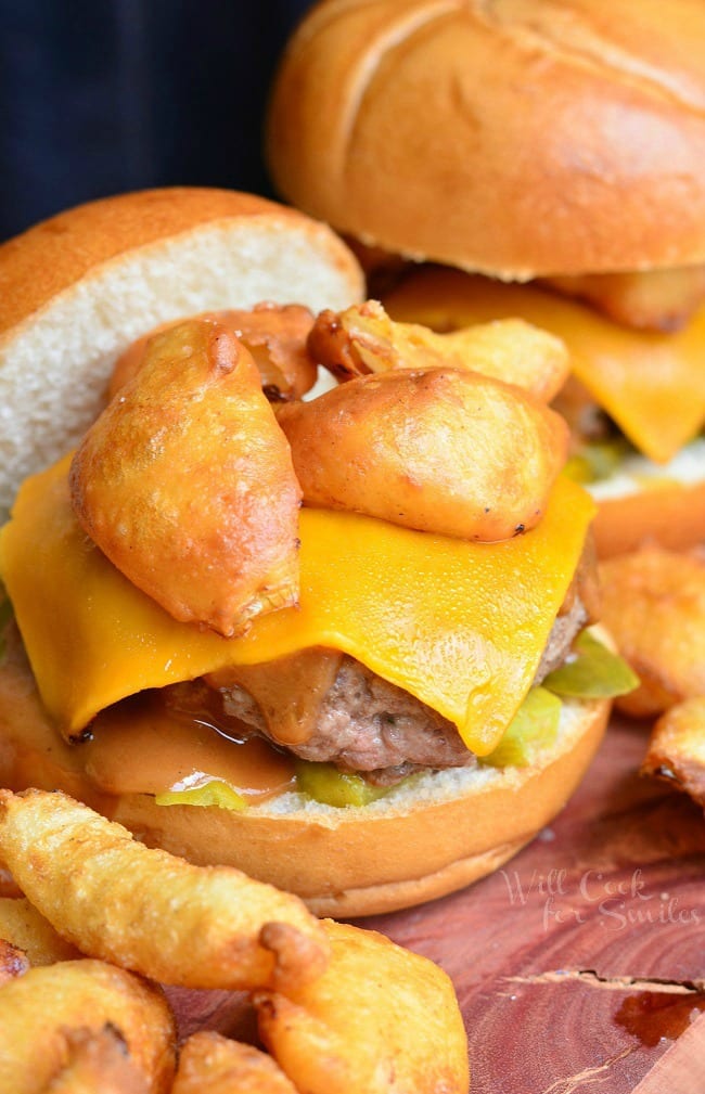 Onion ring bbq cheeseburger on a wooden table with hand battered and fried onion rings in foreground