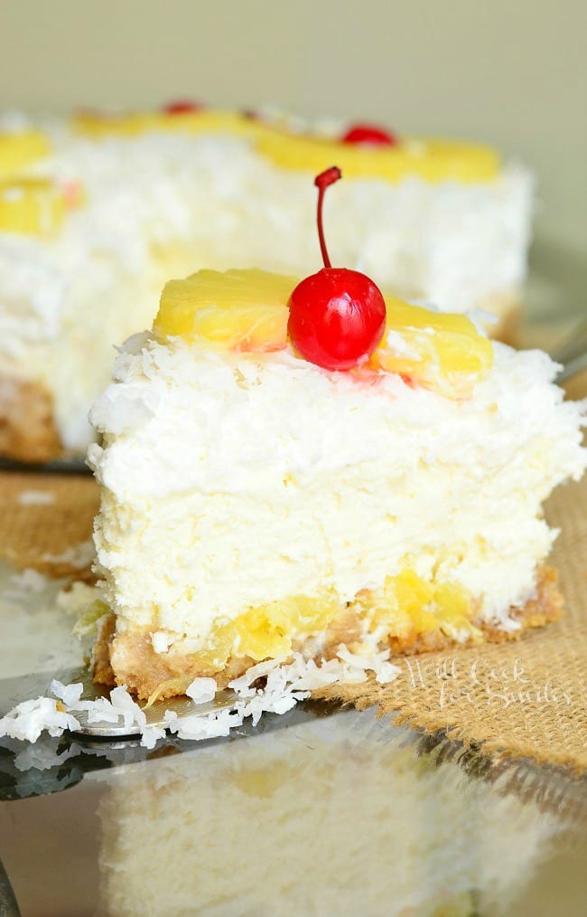 1 slice of pina colada cheesecake in front of the rest of the cake on a tan burlap style placemat