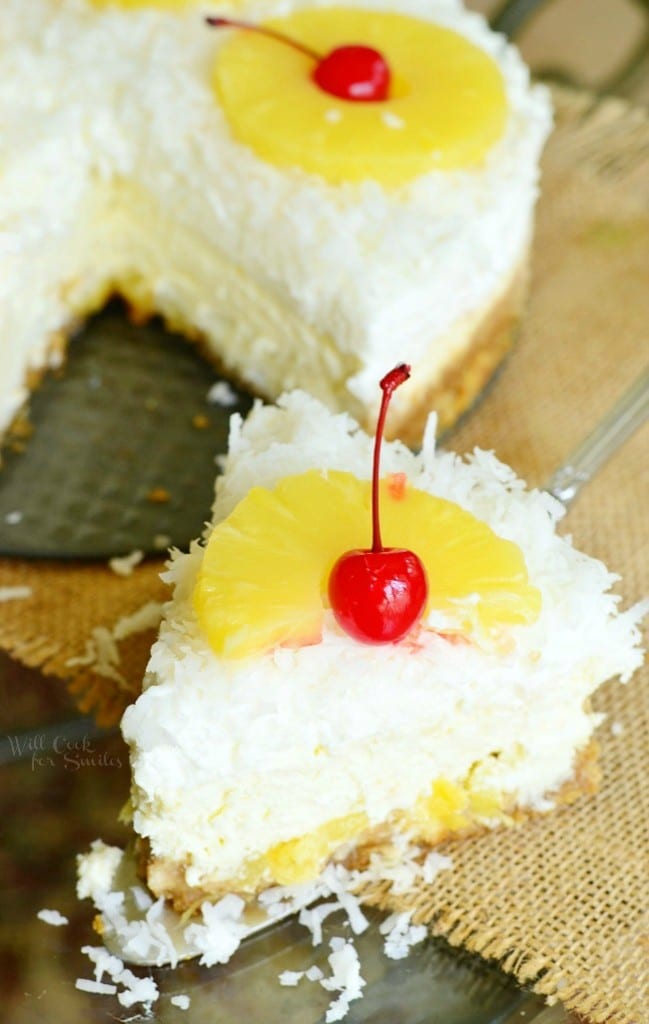view from above of 1 slice of pina colada cheesecake in front of the rest of the cake on a tan burlap style placemat.