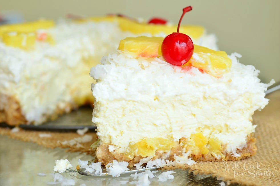 Pina Colada Cheesecake slice on table with coconut, cherry, and pineapple on top 