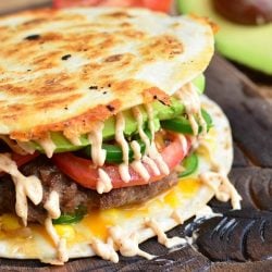 close up view of a View from above of a quesadilla burger on a wooden cutting board with a sliced avocado and tomato in the background