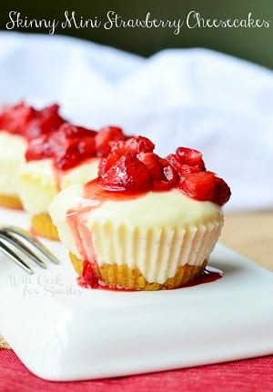 mini strawberry cheesecakes with diced strawberries and sauce on top on a white plate