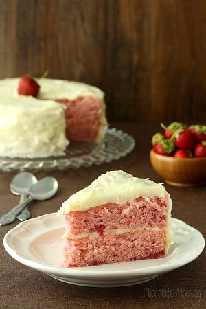 slice of strawberry layered cake with cream cheese frosting on a white plate and the reston a cake stand 