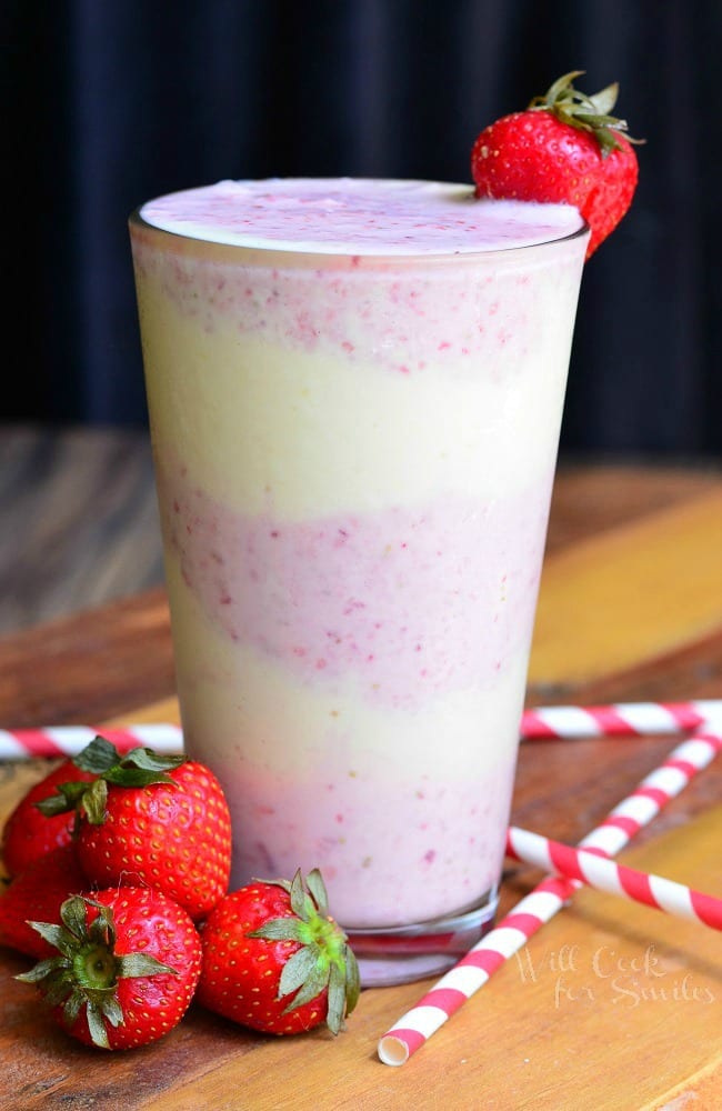 Strawberry Shortcake Milkshake layers of strawberry shake and cake in a tall glass cup with whipped cream and a strawberry as garnish