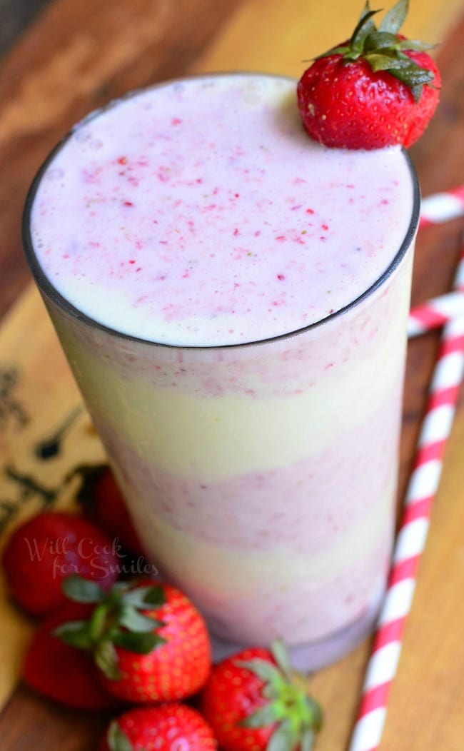 Strawberry Shortcake Milkshake layers of strawberry shake and cake in a tall glass cup with whipped cream and a strawberry as garnish