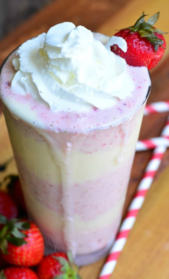 Strawberry Shortcake Milkshake layers of strawberry shake and cake in a tall glass cup with whipped cream and a strawberry as garnish