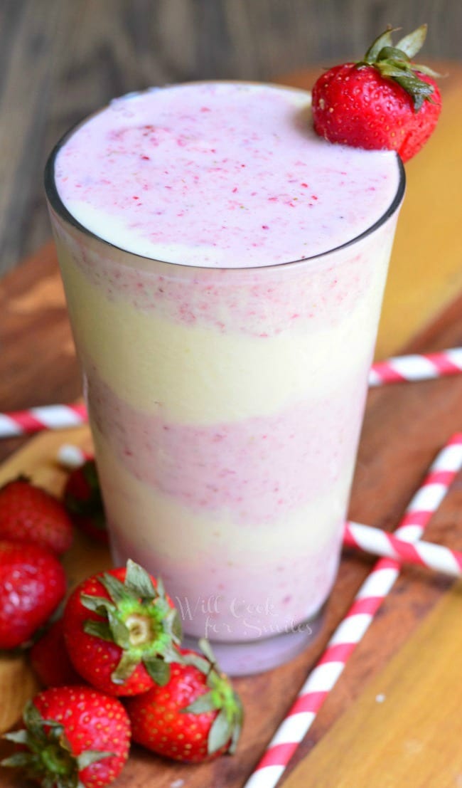 Strawberry Shortcake Milkshake layers of strawberry shake and cake in a tall glass cup with whipped cream and a strawberry as garnish