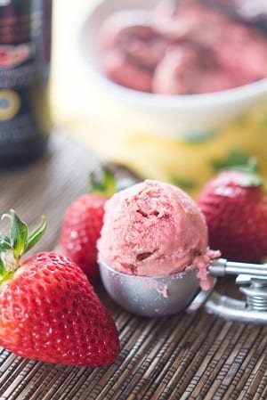 scoop of strawberry ice cream in a metal ice cream scooper with strawberries around it 