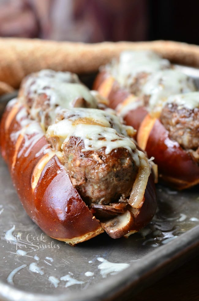 Side view of these Bacon Buffalo Meatball Subs. The juicy meatballs are lined up in a soft pretzel sub roll, baked with sauteed onions, mushrooms and bacon and topped with lots of mozzarella cheese.