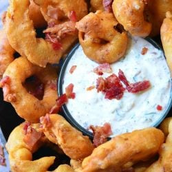 View from above of bacon onion rings with bacon ranch dipping sauce on a black skillet on wooden table