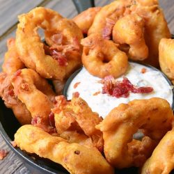 bacon onion rings with bacon ranch dipping sauce on a black skillet on wooden table