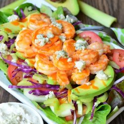 white bowl with homemade blue cheese dressing and a buffalo shrimp salad on a wooden table as seen from above