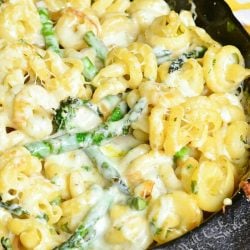 black skillet filled with extra cheesy lemon aspaus pasta on a white and yellow towel on a wooden table as seen from above