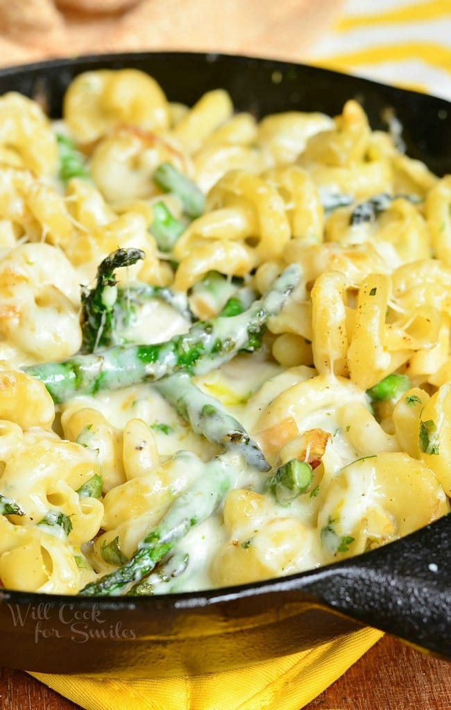 Extra Cheesy Lemon Asparagus Pasta Skillet is presented here in a black skillet. In the skillet, there are many noodles and asparagus covered in a creamy sauce.
