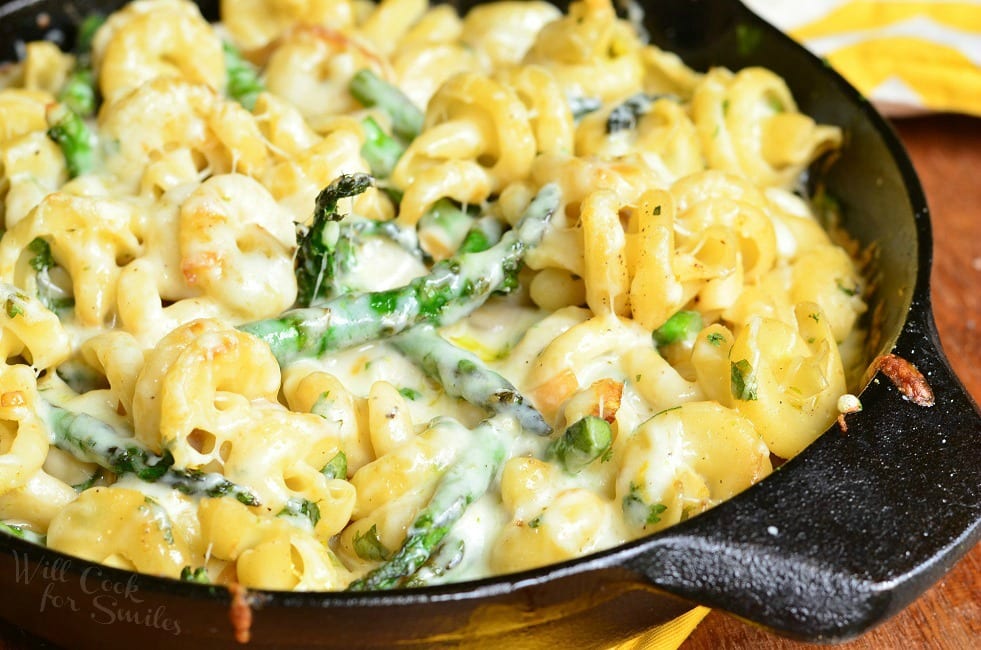 Close up of Extra Cheesy Lemon Asparagus Pasta Skillet presented here in a black skillet. In the skillet, there are many noodles and asparagus covered in a creamy sauce.