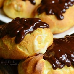 close up view of 2 homemade boston cream eclairs on wooden table in front of white rectangular plate with more eclairs on it