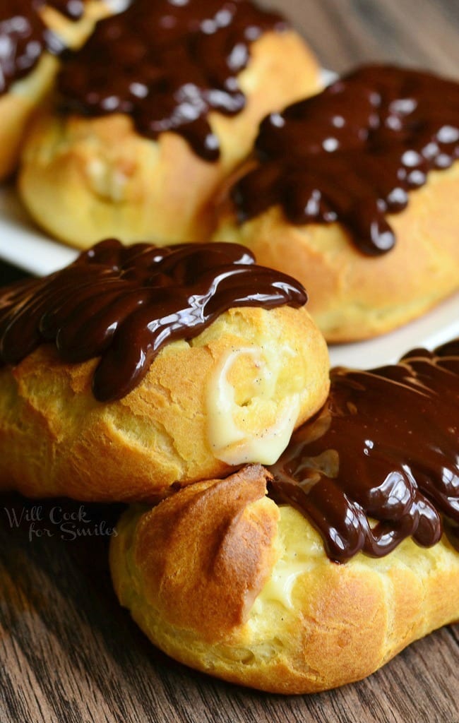 close up view of 2 homemade boston cream eclairs on wooden table in front of white rectangular plate with more eclairs on it