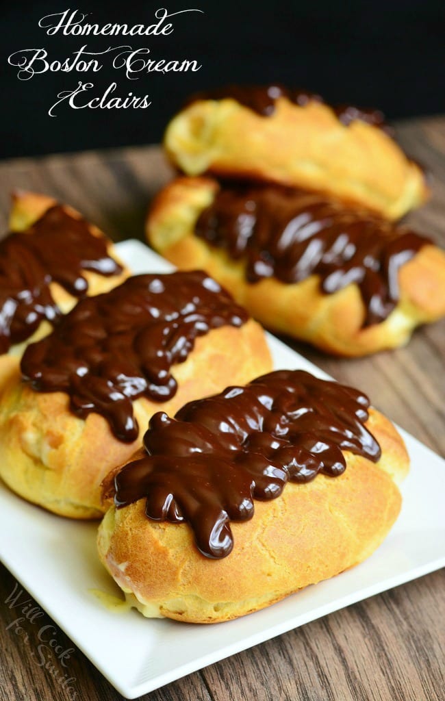 3 boston eclairs with chocolate on top on a plate with 2 on the table behind the plate 