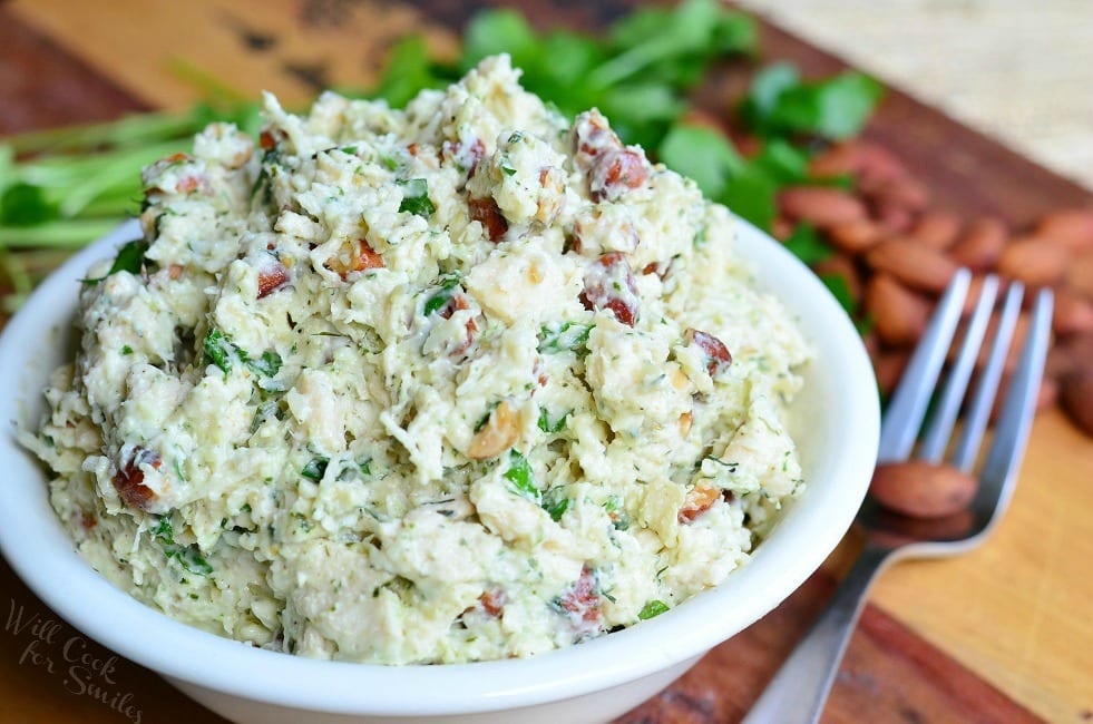 Italian Three Cheese Chicken Salad in a white bowl on a cutting board with a fork to the right side 