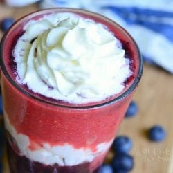 close up view of top of glass with Layered berry daiquiri red white and blue smoothie on a wooden cutting board with blue berries scattered around base of glass