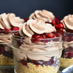 small mason jars filled with no bake chocolate cherry cheesecake on a wooden table with a spoon in the foreground
