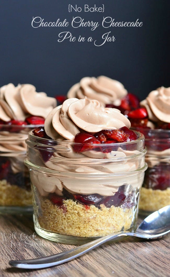 small mason jars filled with no bake chocolate cherry cheesecake on a wooden table with a spoon in the foreground