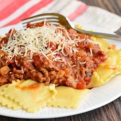 small round white plate with ravioli and meat sauce on a wooden table viewed close up