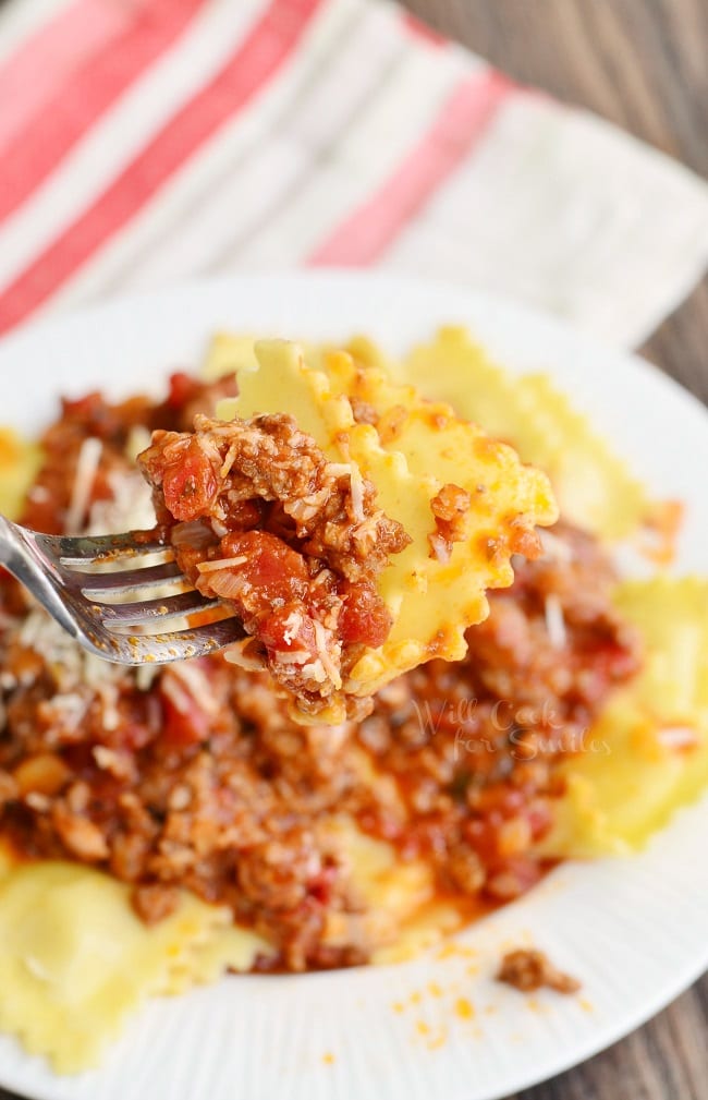 lifting Ravioli up with a fork with Meat Sauce with parmesan cheese on a white plate  