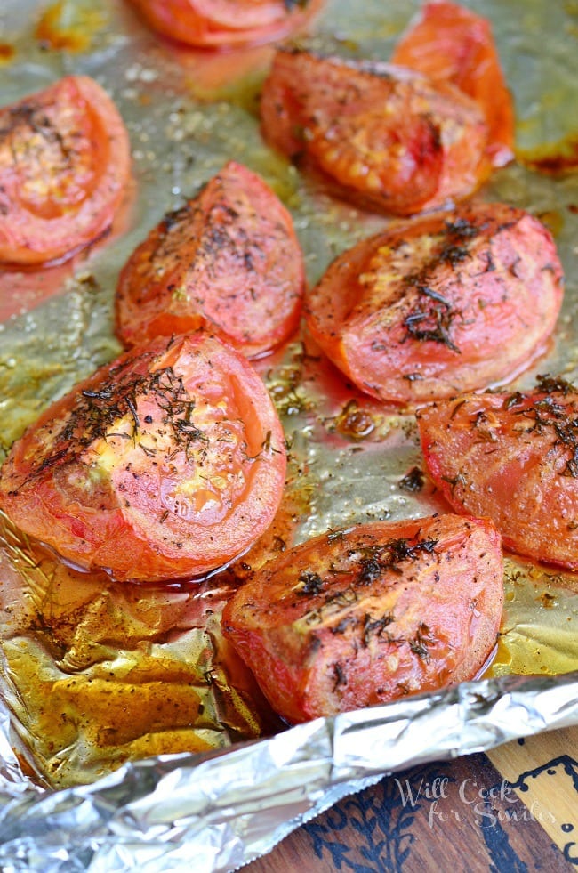 Roasted Tomatoes are lined on a pan covered with tin foil. They are topped with dill weed.