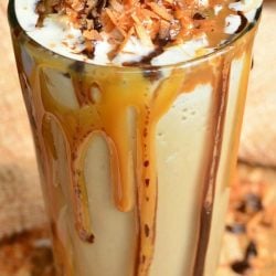 pint glass filled with samoas frozen coffee on a wooden table with coconut shaving scattered around the bottom of the glass