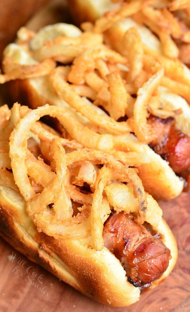 Fried Onions and Hot Dogs in a bun on a wood cutting board 