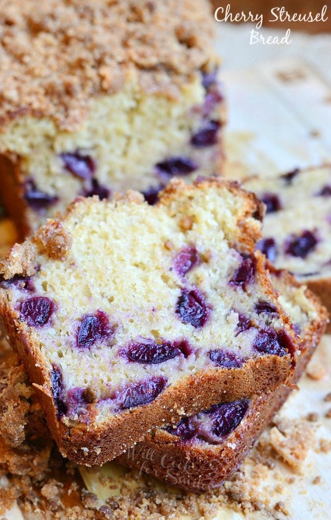 A few pieces of Cherry Streusel Bread have been cut from the loaf. The cut pieces lay stacked on each other in front of the loaf. The streusel is on top of the bread and laying around the bread slices. 