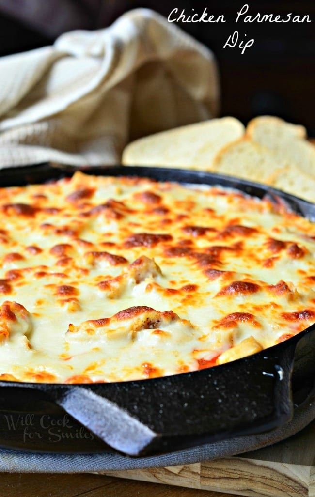 Chicken Parmesan Dip in a black skillet. The top is cheese that has been browned to perfection. Pieces of bread are in the background.