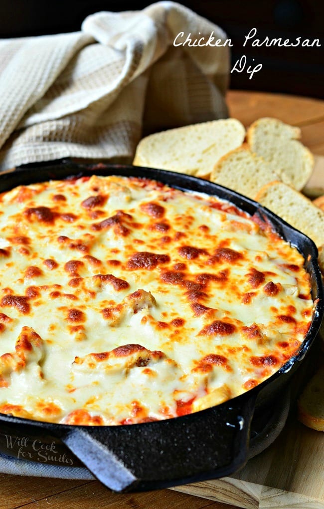 Chicken Parmesan Dip in a black skillet. The top is cheese that has been browned to perfection. Slices of bread are behind the skillet.