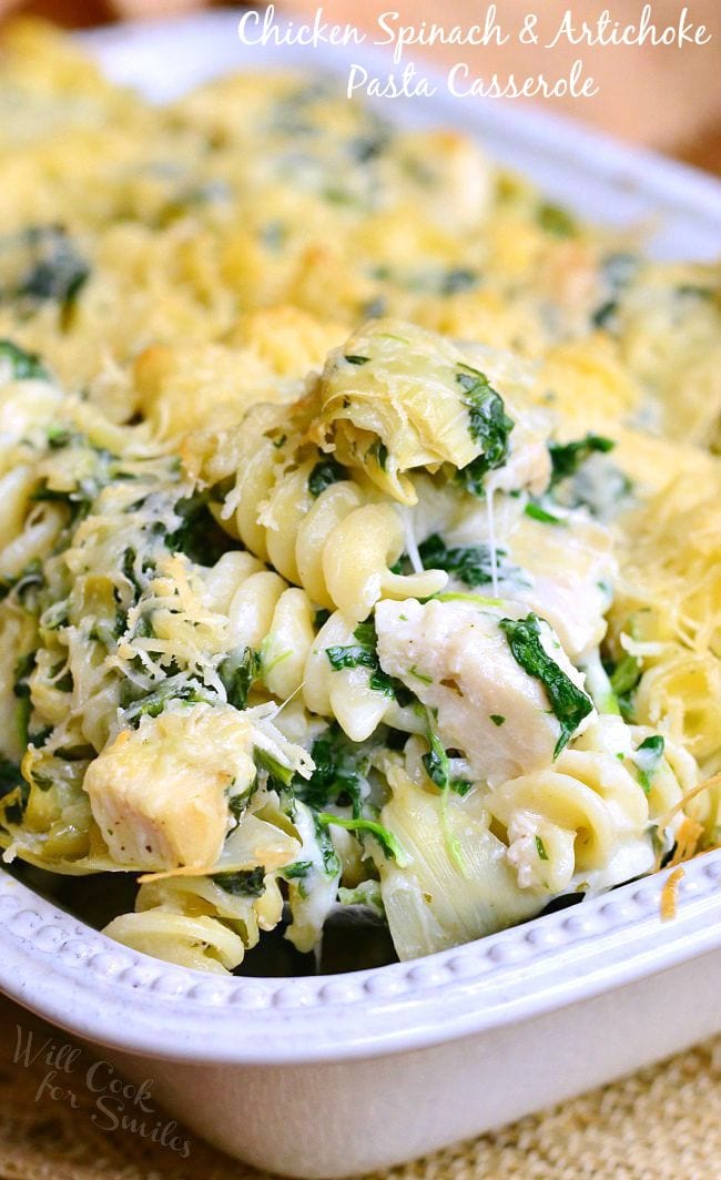 Close up of Chicken Spinach and Artichoke Pasta served in a white casserole dish.