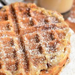 3 stacked cinnamon peach oat waffles on a white plate with a glass of coffe in the background