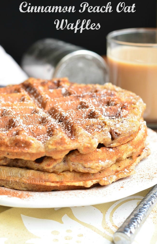 Three Cinnamon Peach Oat Waffles stacked on top of each other served on a white plate. Waffles are sprinkled with cinnamon and powder sugar.