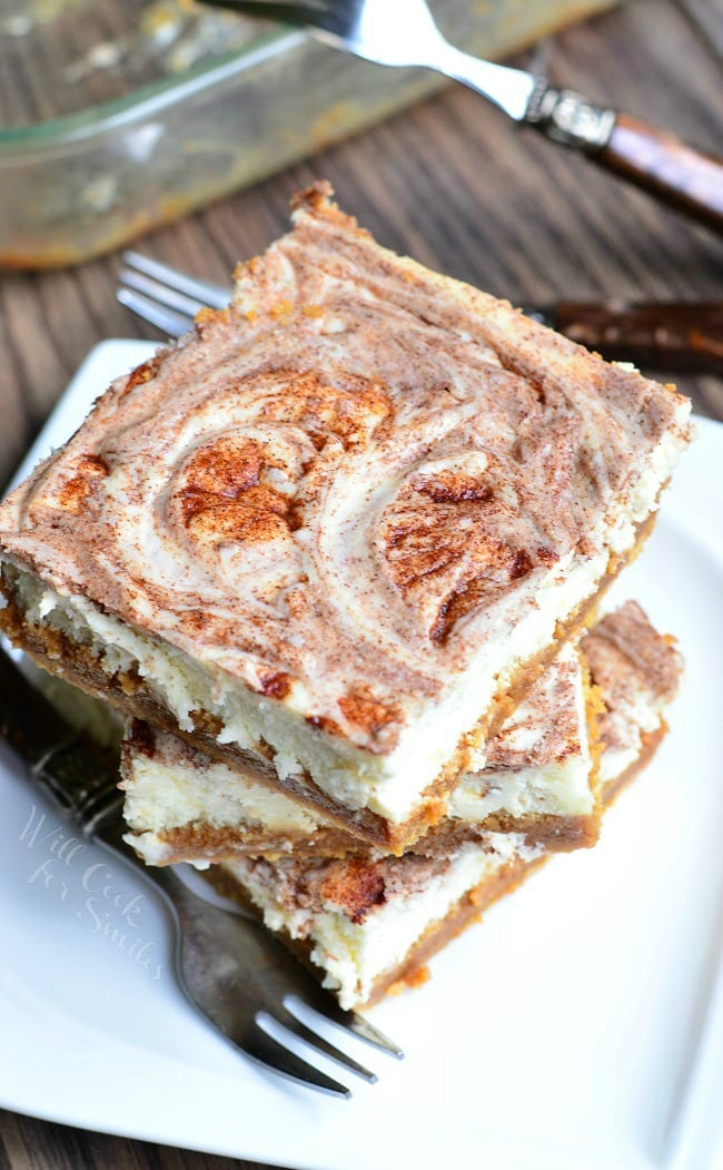 Several Caramel Cinnamon Swirl Cheesecake Bars are stacked on a small, white plate. A fork lays on the plate as well.