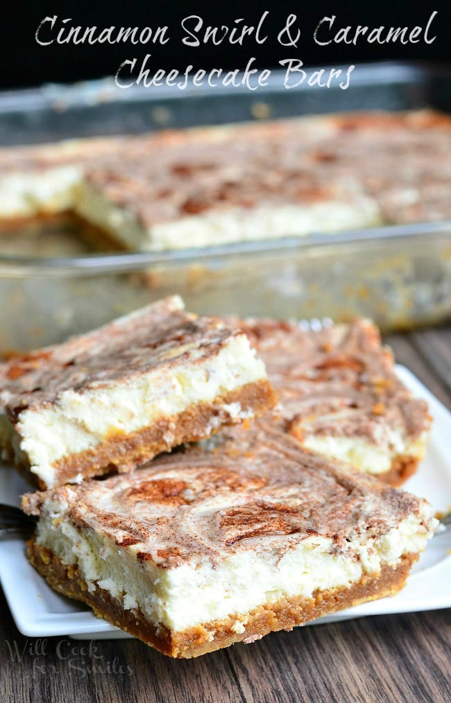 Several Caramel Cinnamon Swirl Cheesecake Bars lay on a small, white plate. The glass baking dish with the remaining cheesecake bars fades into the background.