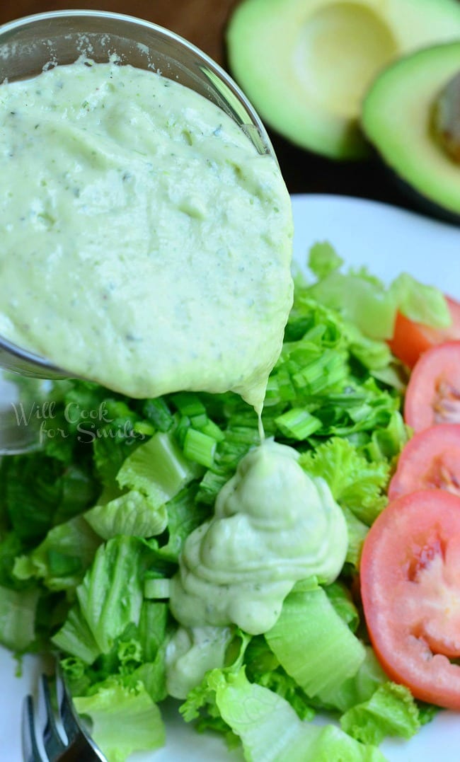 The Creamy Avocado Dressing is being poured from the glass pouring dish onto a bed of chopped lettuce.