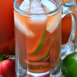 Clear glass beer mug filled with strawberry lime infused iced tea in front of another mug and pitcher filled with tea