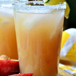 2 pint glasses filled with white peach margarita on a wooden serving tray wtih slice peaches in foreground