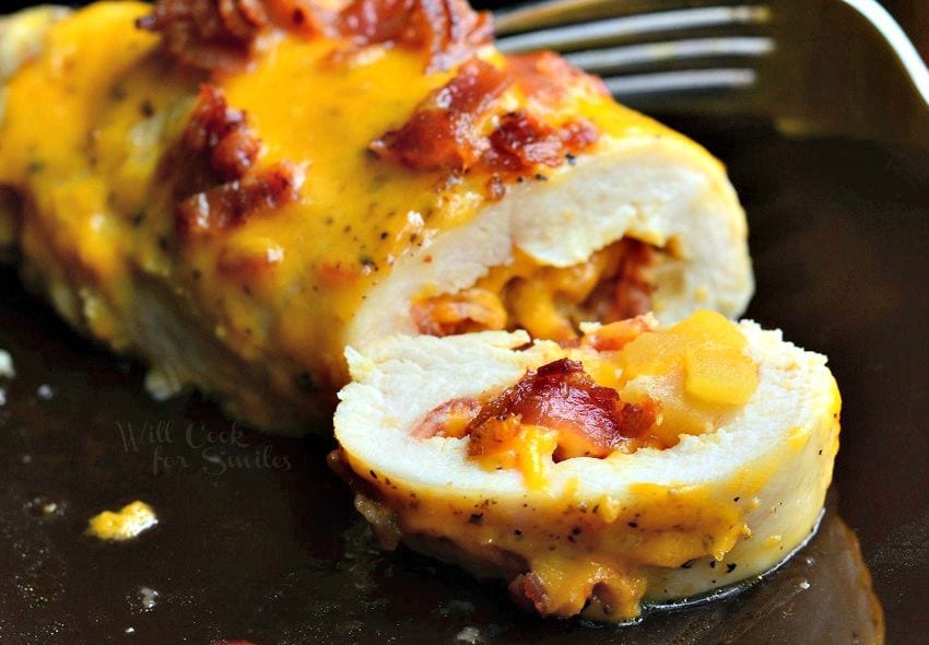 Sliced chicken breast that's been stuffed with apples, bacon, and cheese. Melted cheese and bacon also appear on top of the chicken breast.