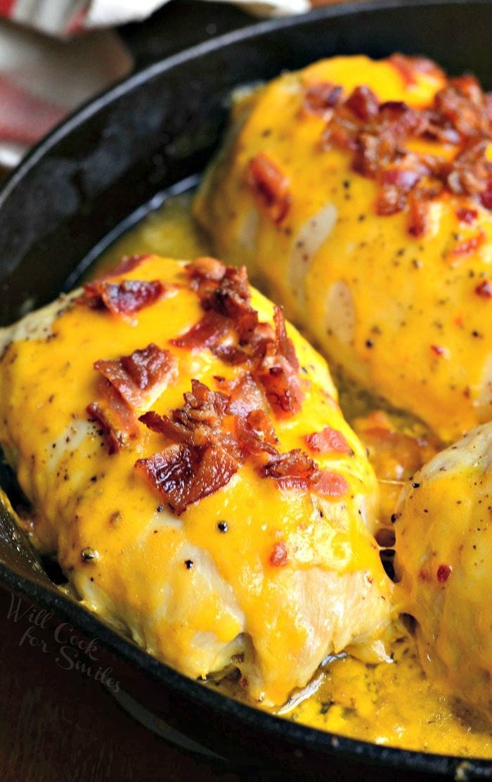 Apple Bacon Cheddar Stuffed Chicken in a black skillet covered in melted cheese and bacon.