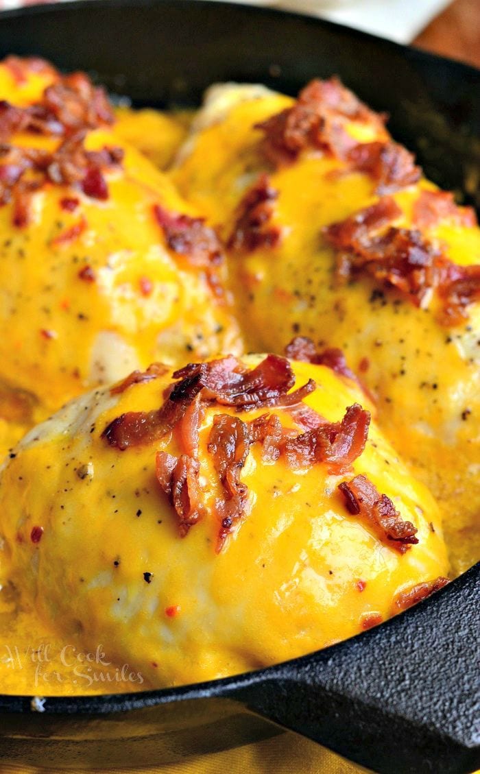 Apple Bacon Cheddar Stuffed Chicken in a black skillet covered in melted cheese and bacon.