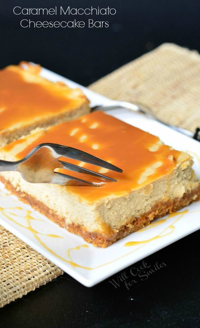 Caramel Macchiato Cheesecake Bars are on a white plate. Caramel is drizzled on top of the bars, as well as on the plate. A fork is inserted into one of the bars.