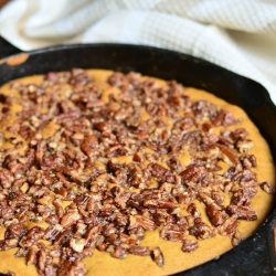 black skillet with a giant pumpkin cookie while sitting on a wooden table with a white cloth in the background